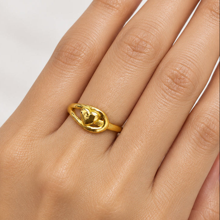 A close-up of a hand wearing a polished yellow gold ring with a stylized heart design on a white background.