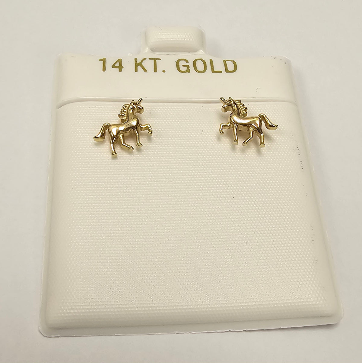 A pair of small gold unicorn stud earrings displayed on a white jewelry card labeled '14 KT. GOLD'.